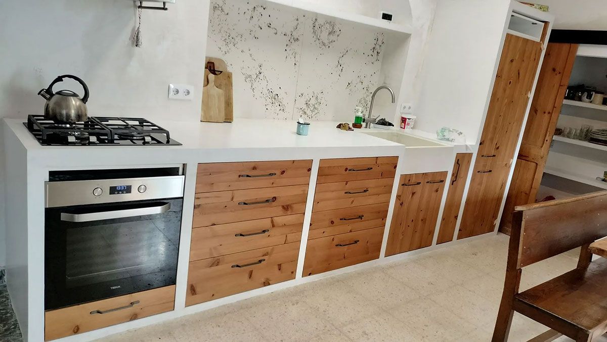 Cocina con encimeras blancas, gabinetes de madera, horno, estufa y fregadero.