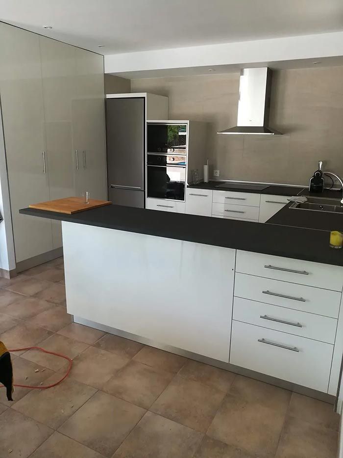 Cocina blanca moderna con isla, encimeras grises, electrodomésticos de acero inoxidable y piso de baldosas.