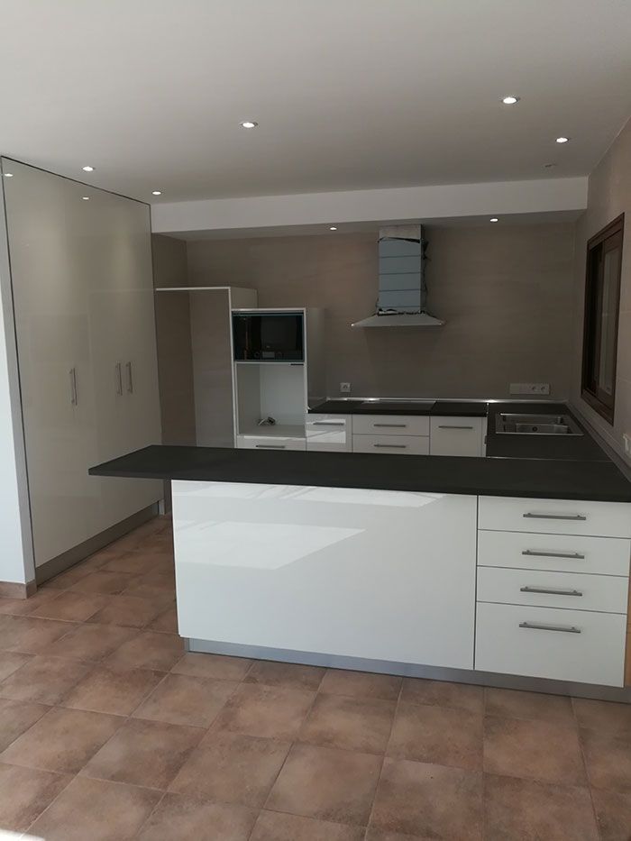 Cocina blanca moderna con isla, encimera oscura, gabinetes y electrodomésticos.