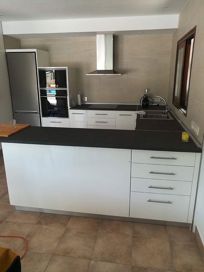 Cocina blanca moderna con encimeras negras, electrodomésticos de acero inoxidable y placa para salpicaduras de azulejos.