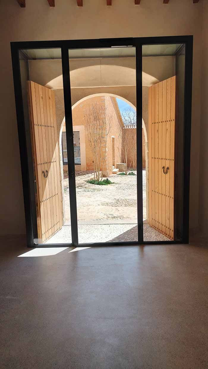 Puertas de madera que dan a un patio soleado. Entrada arqueada y luz natural.