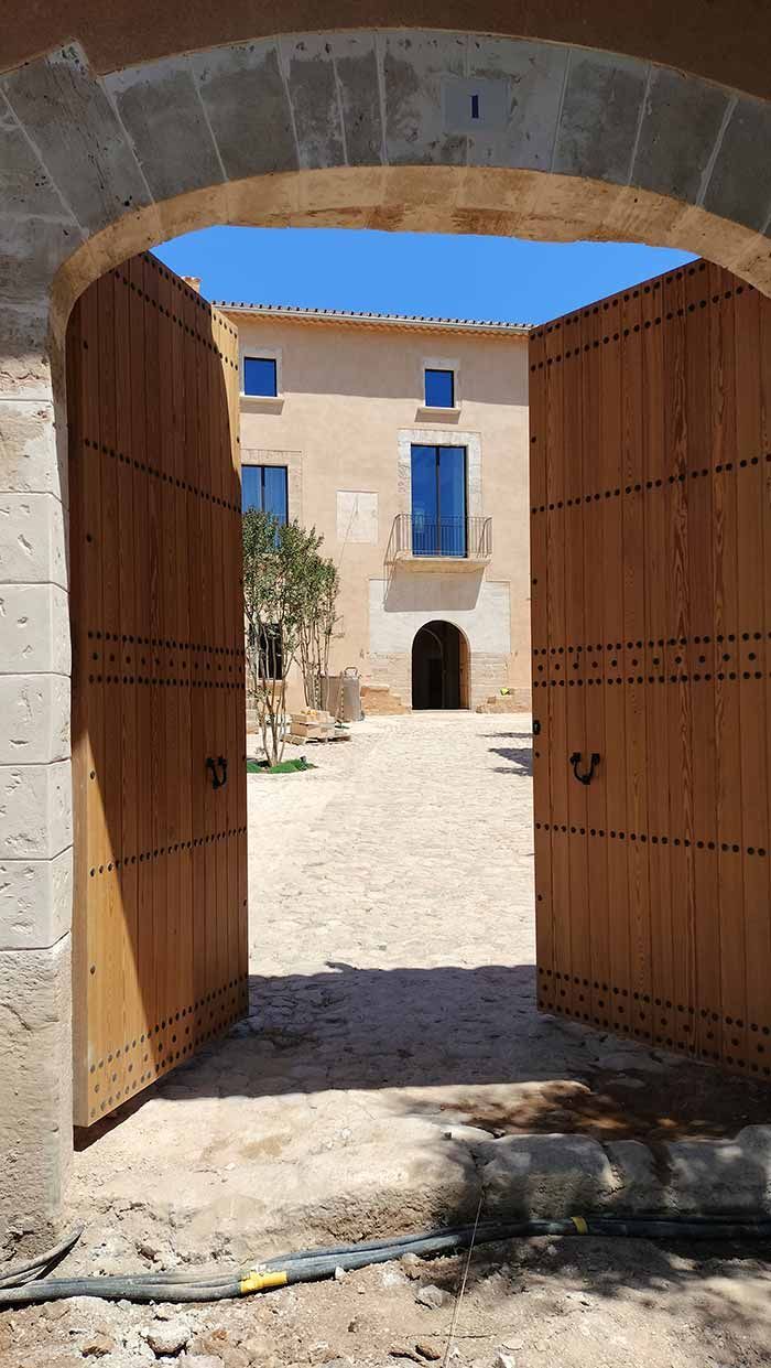 Unas puertas de madera dan a un patio. Se ve un edificio con entrada arqueada y marcos de ventanas azules.