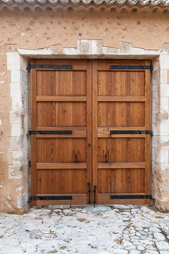Puertas dobles de madera con bisagras de metal negro en un edificio de piedra.