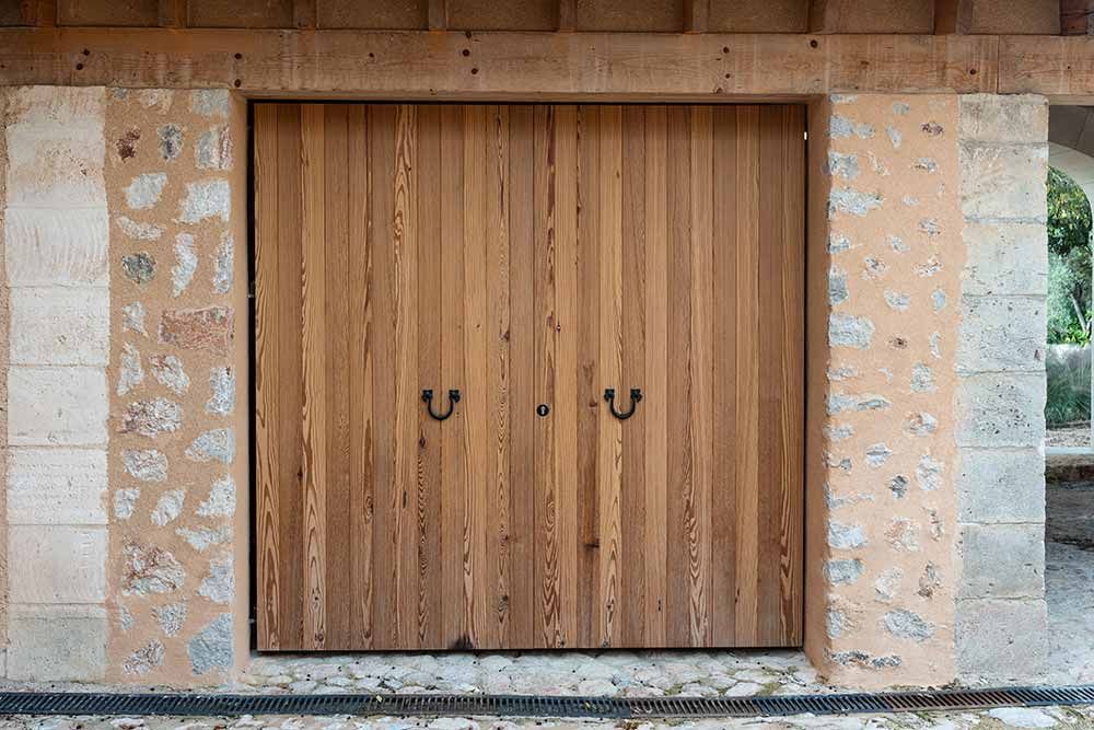 Puertas dobles de madera con tiradores de metal oscuro engastados en una pared de piedra y estuco.