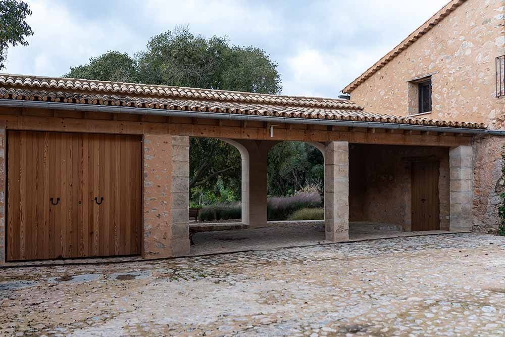 Edificio de piedra con garaje al aire libre. Puertas de garaje de madera, techo de tejas y suelo de adoquines.