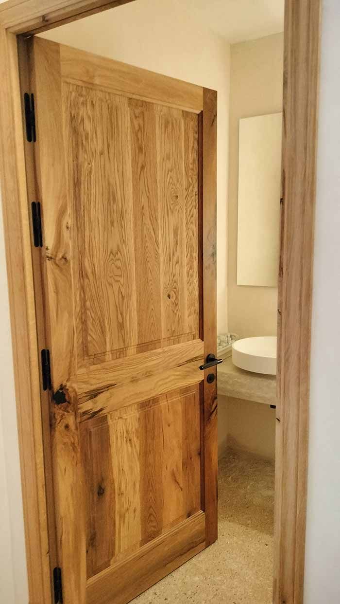Puerta de madera abierta a un baño con lavabo y espejo.