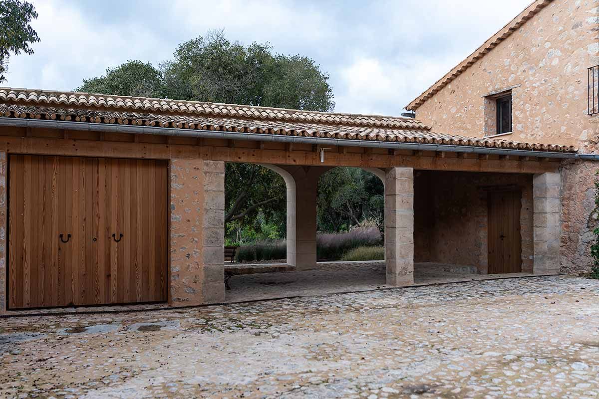 Cochera de piedra con puertas de madera y aberturas arqueadas, bajo un techo de tejas de barro.