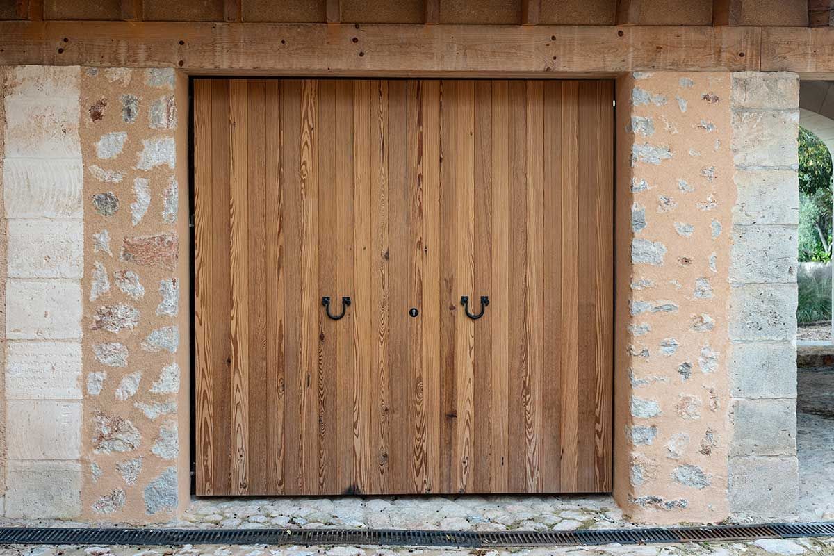 Puertas dobles de madera con tiradores oscuros colocadas en una pared de piedra.