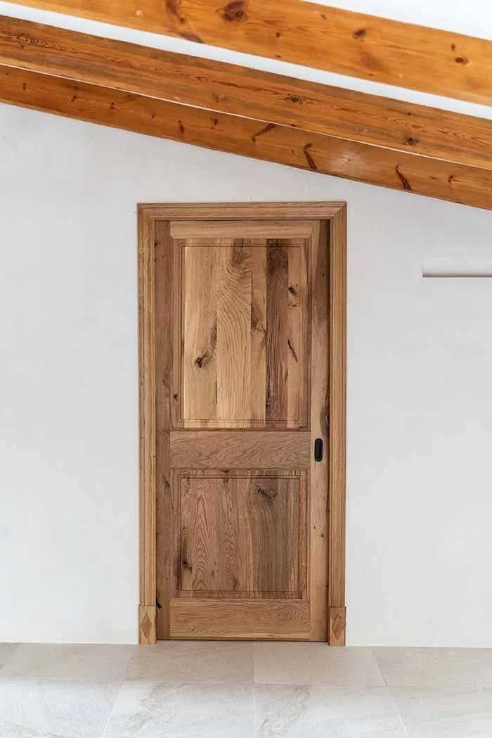 Puerta de madera en habitación de paredes blancas con vigas de madera en el techo.