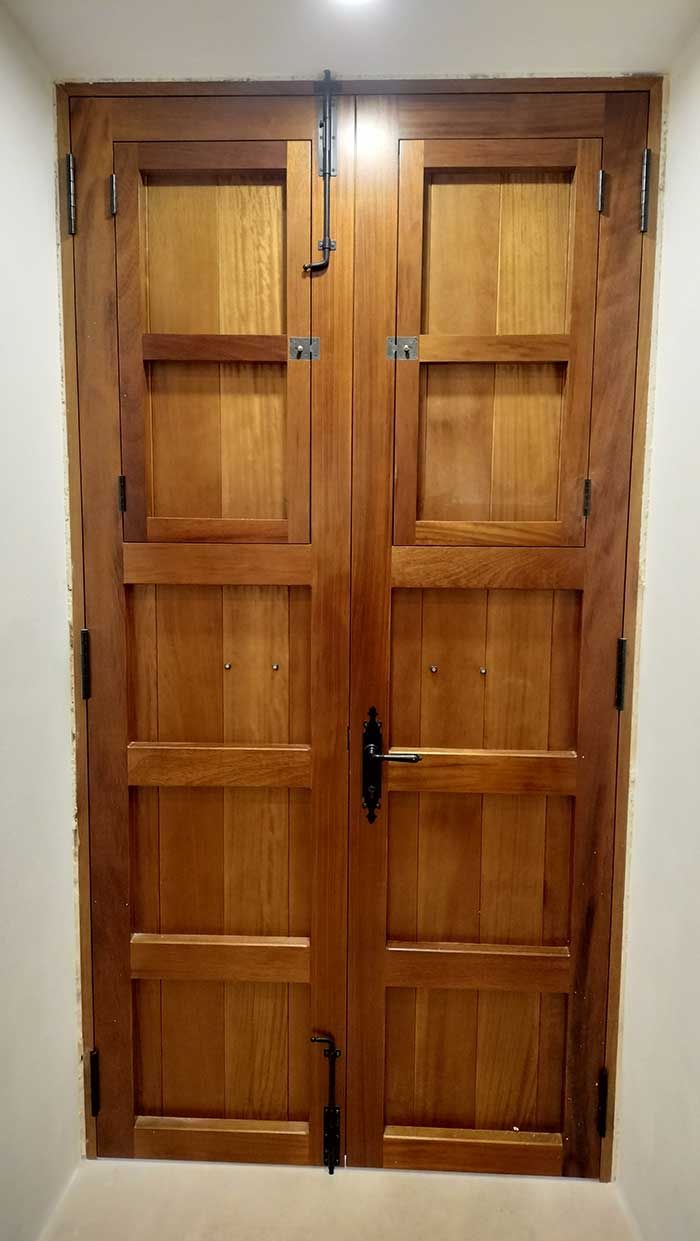 Puertas dobles de madera con herrajes oscuros, colocadas en una entrada de color claro.