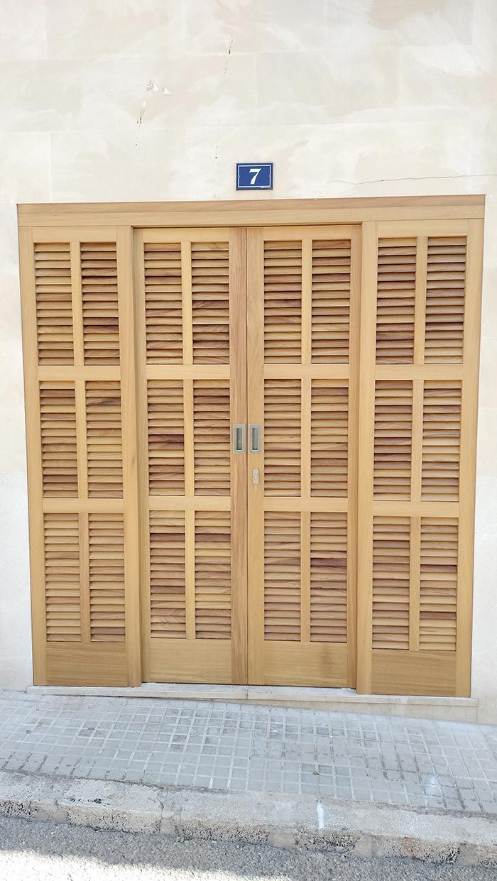 Puertas de madera con contraventanas y un número de casa 7 encima, en una pared de color beige claro.