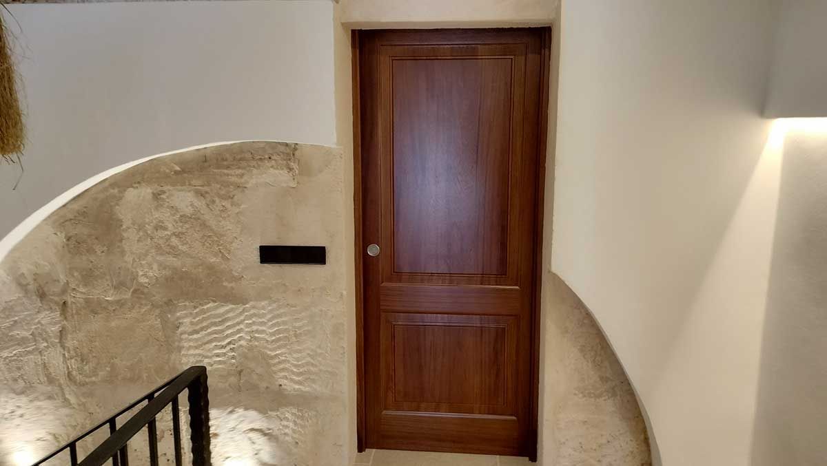 Puerta de madera con pomo, colocada en una pared de piedra curva de color claro.