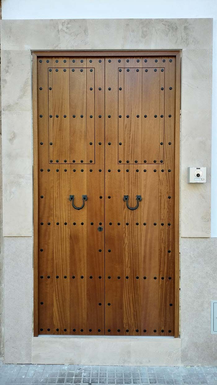 Puertas dobles de madera con montantes metálicos, tiradores de aro y marco de piedra.