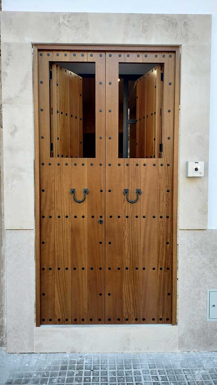 Puertas dobles de madera con montantes metálicos, contraventanas abiertas y marco de piedra.