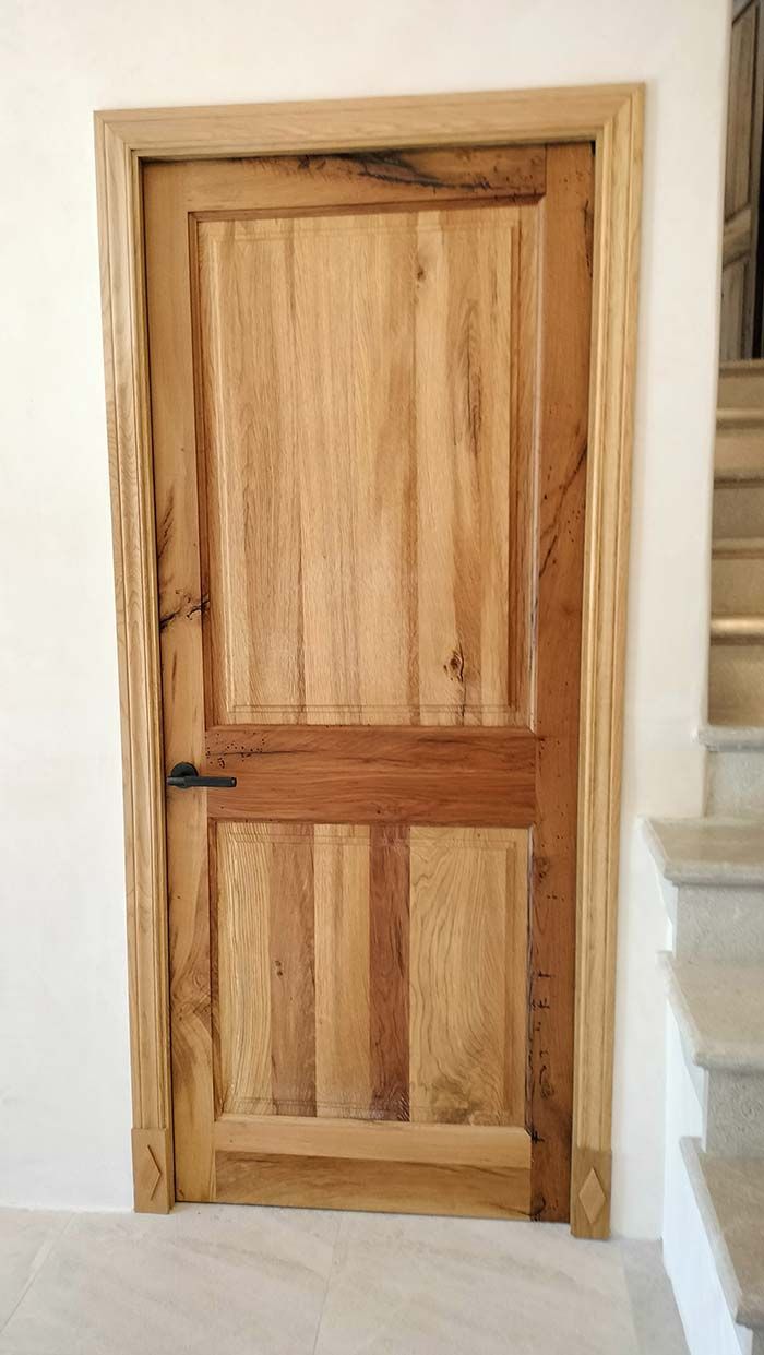 Puerta de madera con tirador oscuro, colocada en un marco de color claro sobre una pared blanca; escaleras a la derecha.