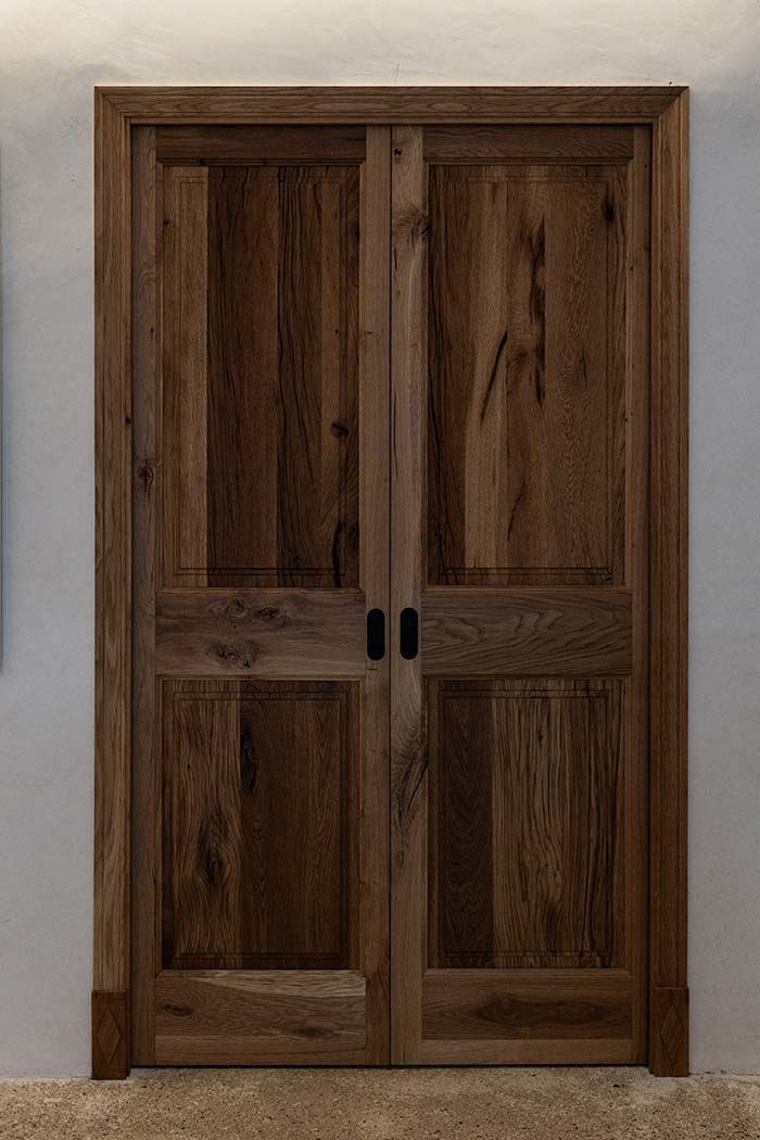Puertas dobles de madera con tiradores oscuros contra una pared clara.