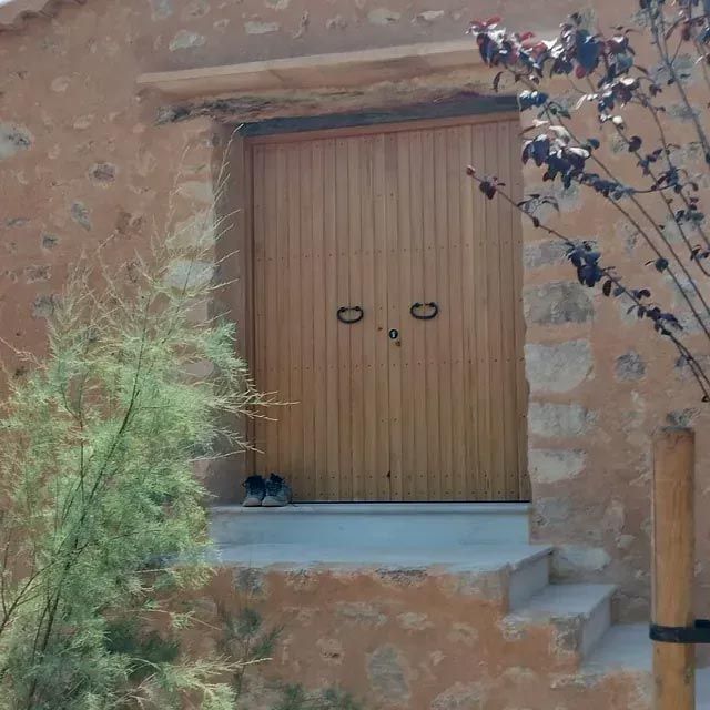 Puertas dobles de madera con manijas oscuras en un edificio de piedra, escalones que conducen hacia arriba.