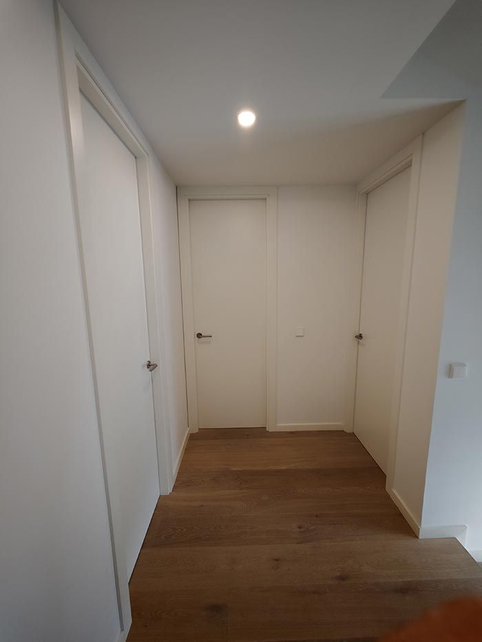 Pasillo con tres puertas blancas y suelo de madera, iluminado por lámpara de techo.