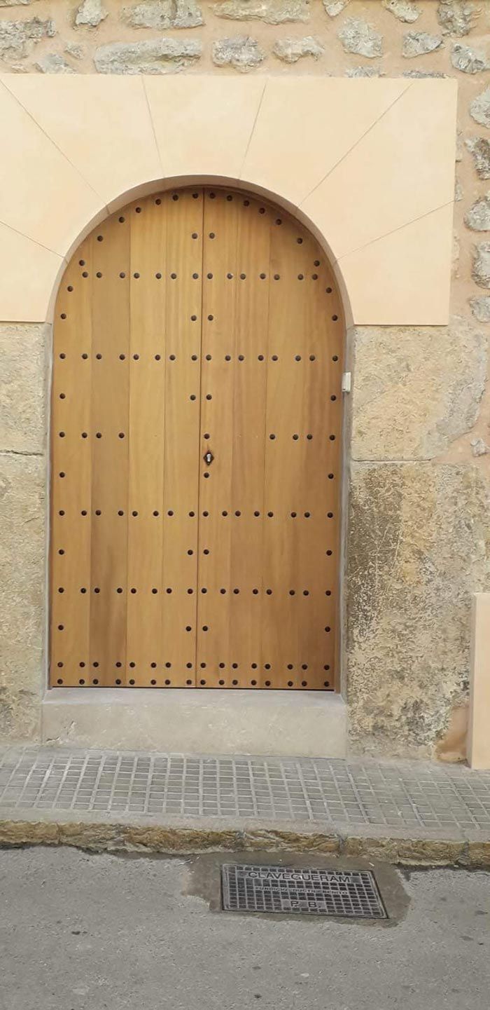 Puerta arqueada de madera con montantes de latón incrustados en una pared de piedra.
