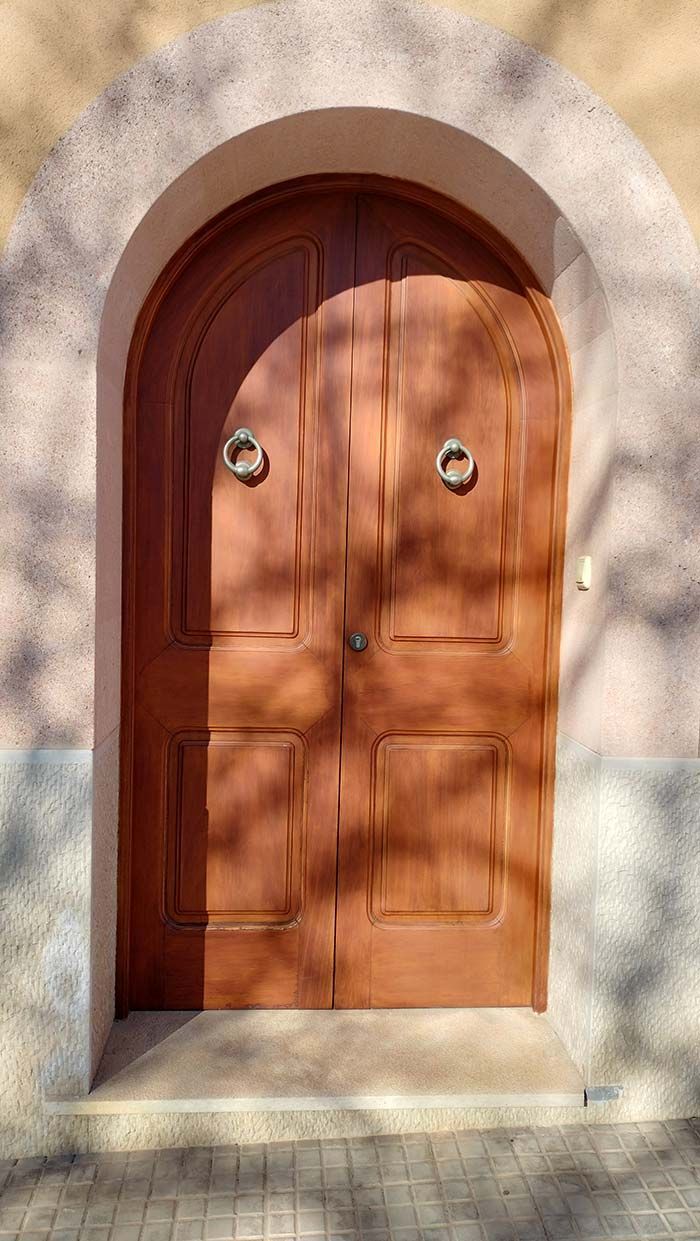 Puerta doble arqueada de madera con aldabas de aro metálico.