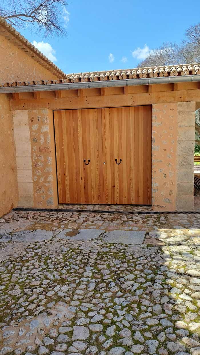 Puertas dobles de madera en arco de piedra con suelo adoquinado.