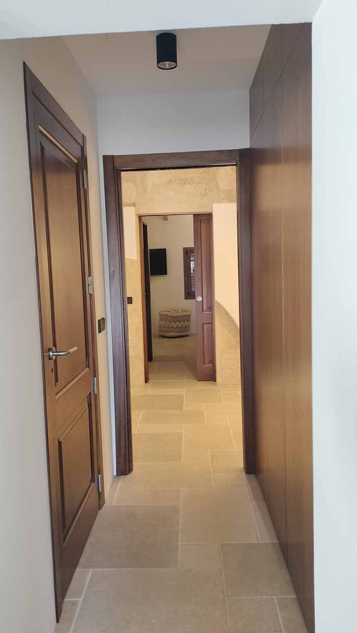 Pasillo estrecho con suelo de piedra y tres puertas marrones que conducen a otras habitaciones.