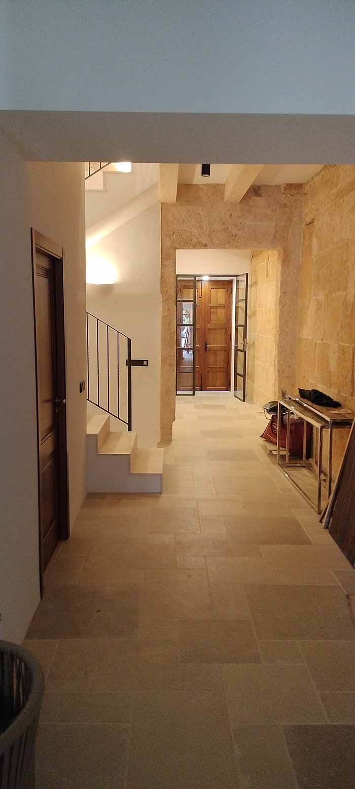 Pasillo con suelo de piedra, escaleras a la izquierda y puerta de madera al final del pasillo.