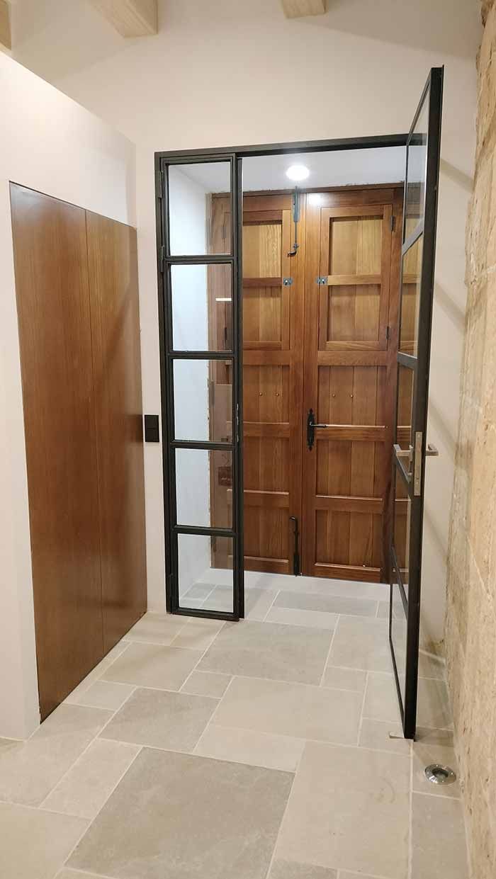 Pasillo con puertas de madera y cristal. Una puerta está cerrada. Suelo de baldosas. Paredes de color claro.