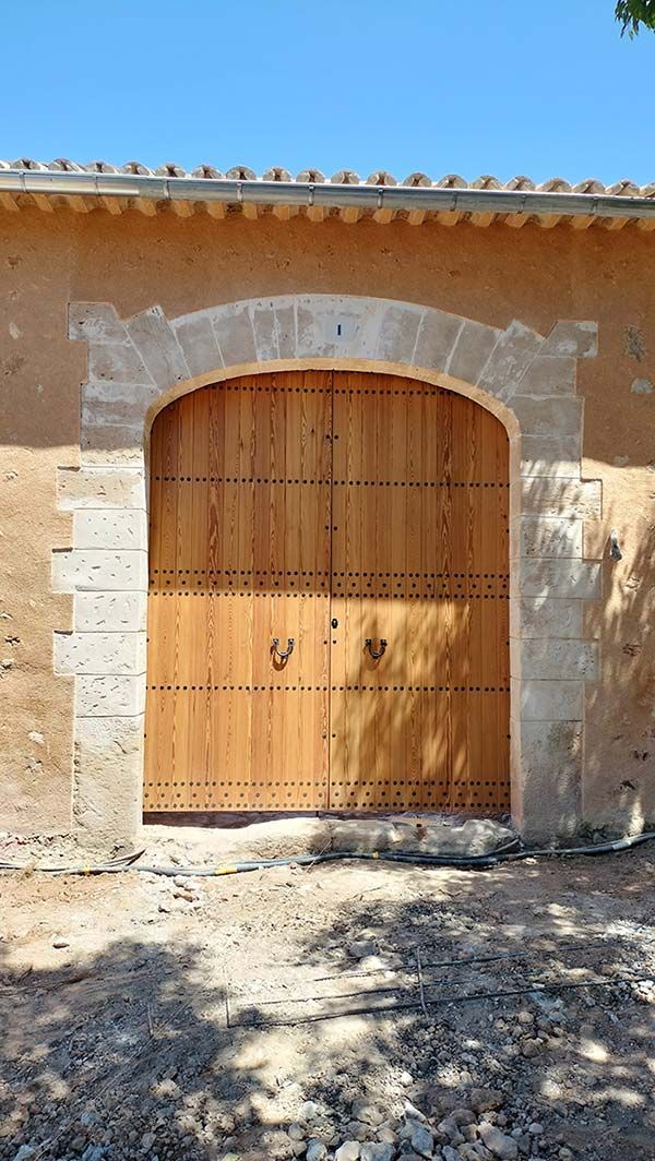 Puertas dobles de madera con montantes metálicos colocados en un arco de piedra marrón claro en una pared marrón claro.