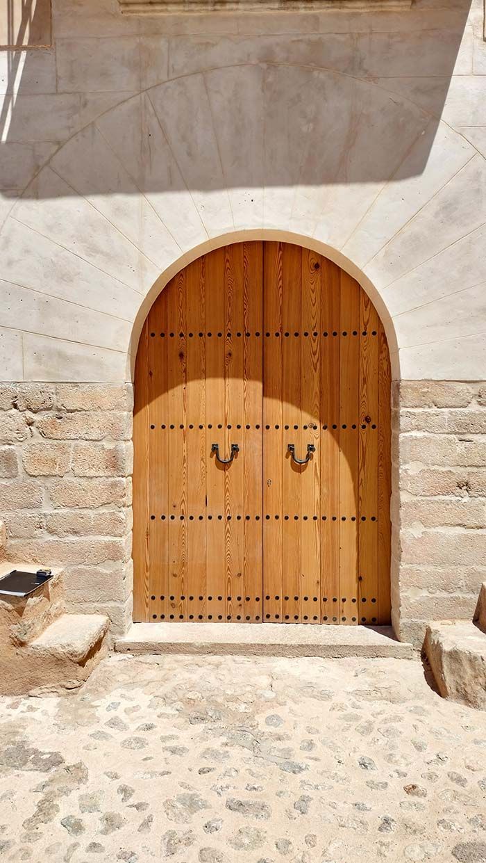 Puerta arqueada de madera con manijas de latón colocadas en pared de piedra.