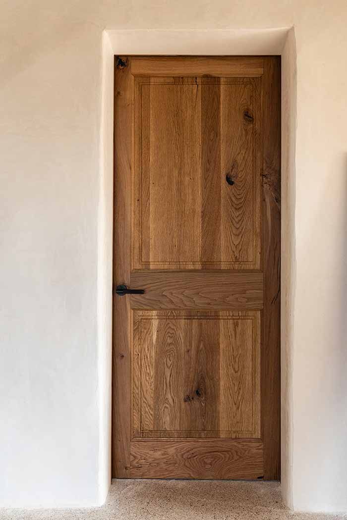 Puerta interior de madera con tirador negro encastrada en pared blanca.