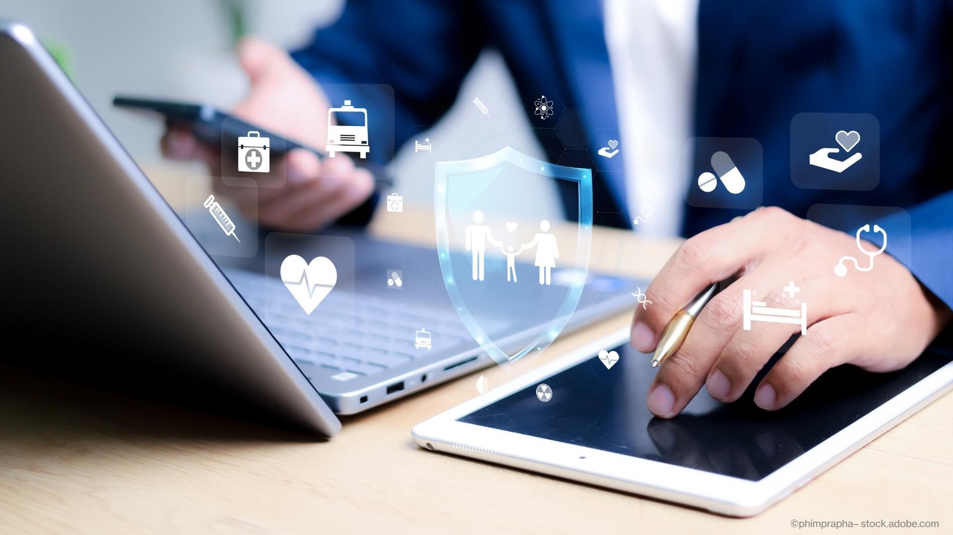 Eine Person sitzt mit einem Handy und einem Tablet an einem Laptop