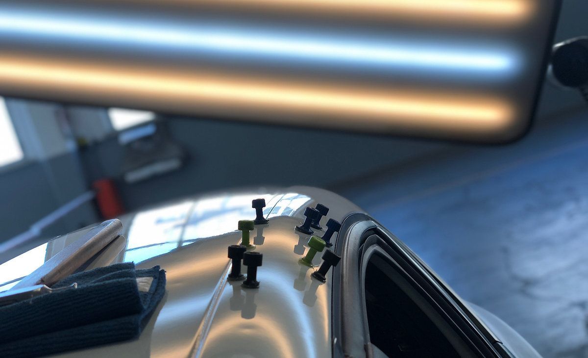 Techo brillante de un coche con pequeñas figuras de juguete, bajo luces horizontales brillantes en un garaje.