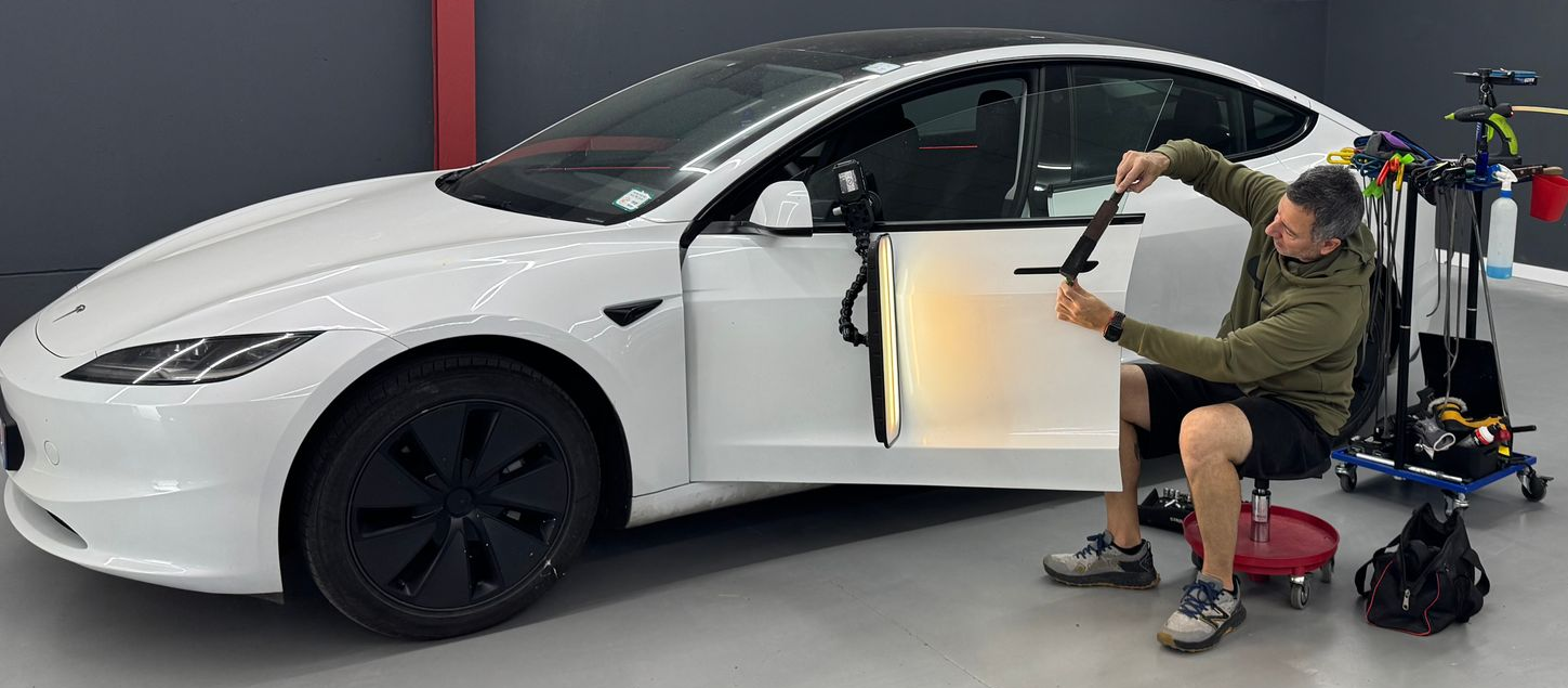 Persona trabajando en la puerta abierta de un coche deportivo blanco en un garaje.