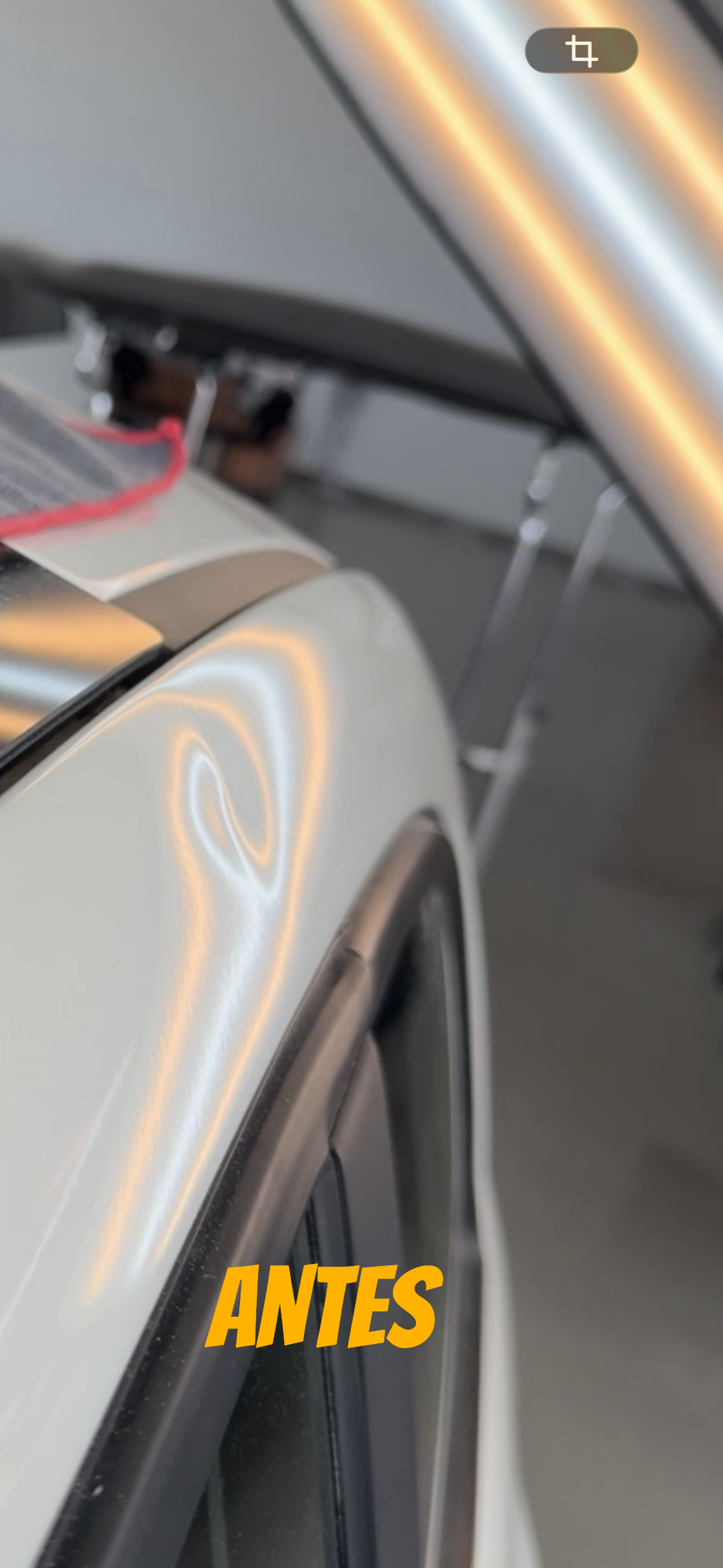 Primer plano del capó blanco de un coche en un garaje, con reflejos de luz naranja y una etiqueta amarilla con la inscripción