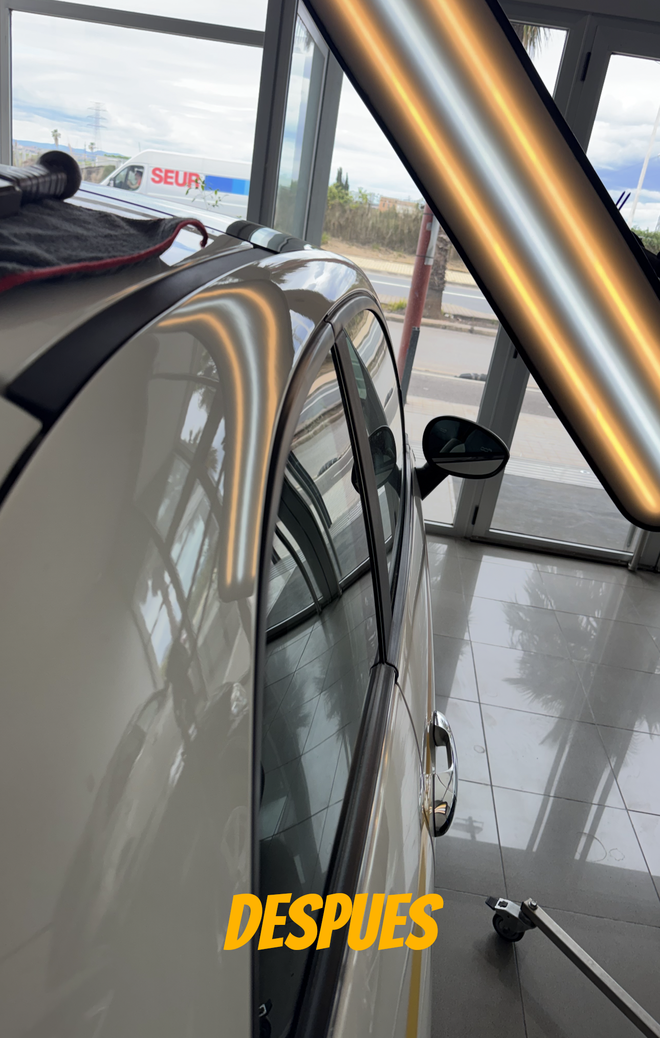 Primer plano del panel lateral de un coche blanco que está siendo pulido junto a vigas metálicas, con la palabra