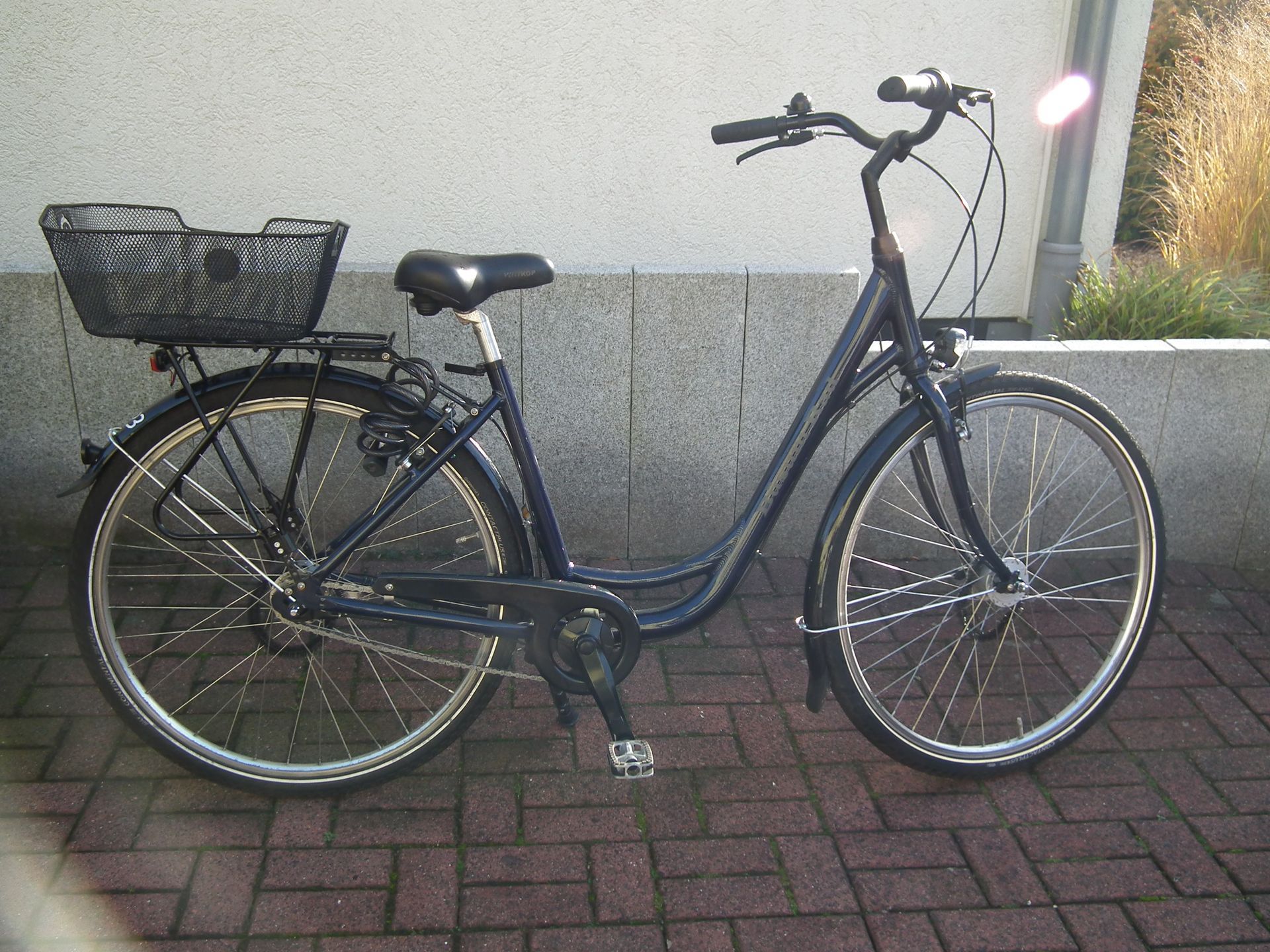 Ein Fahrrad mit einem Korb auf der Rückseite steht auf einem gepflasterten Gehweg