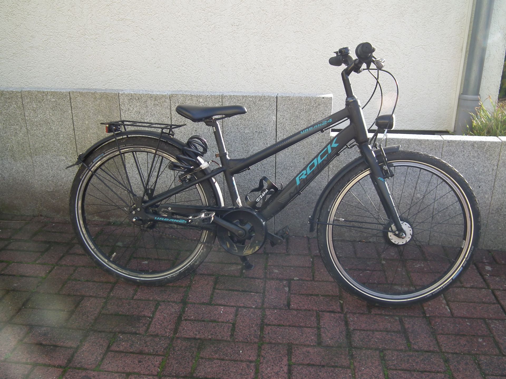 Ein schwarzes Fahrrad steht auf einem gepflasterten Gehweg vor einem Gebäude.