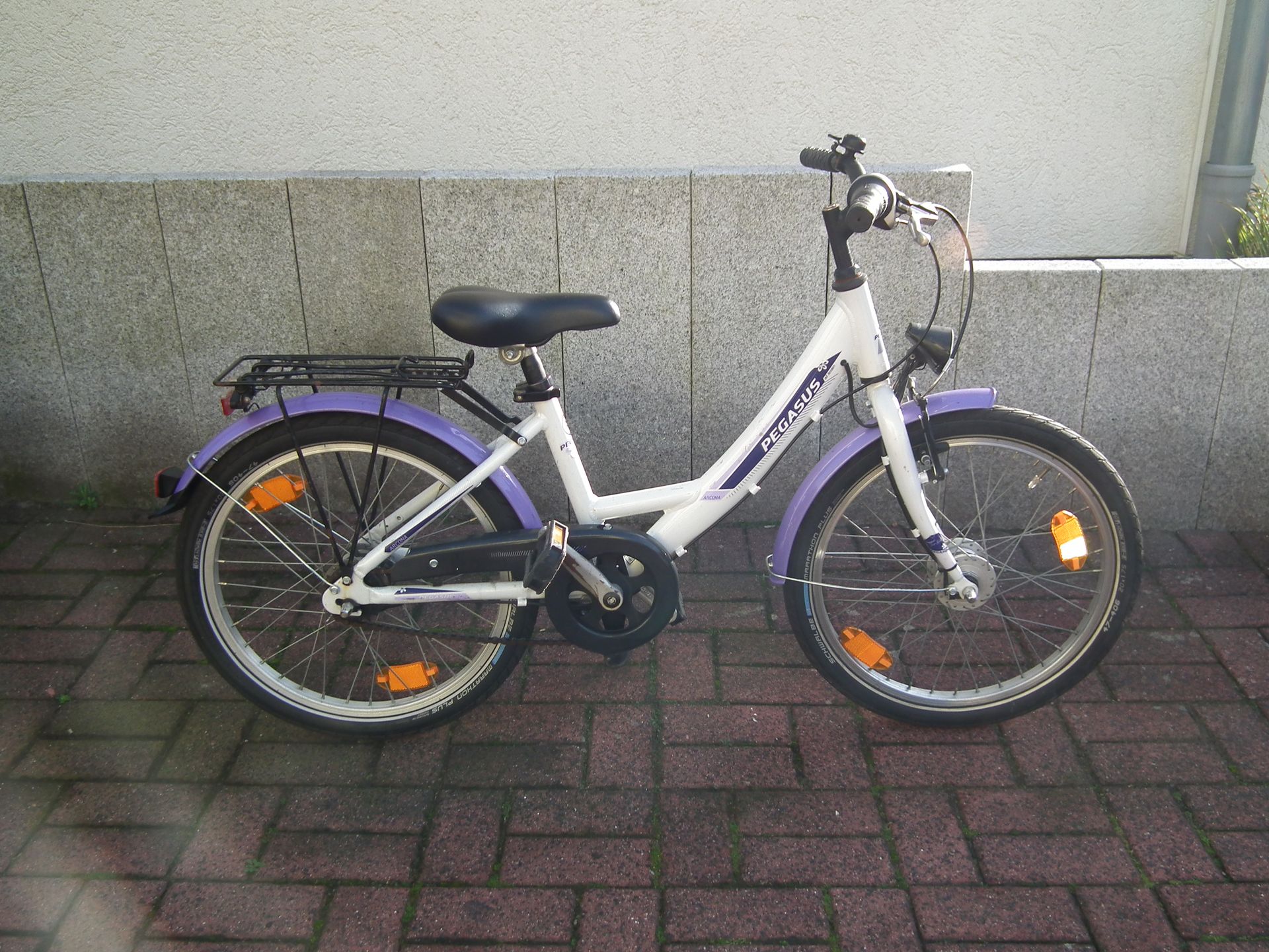 Ein weiß-lila Fahrrad steht auf einem gepflasterten Gehweg