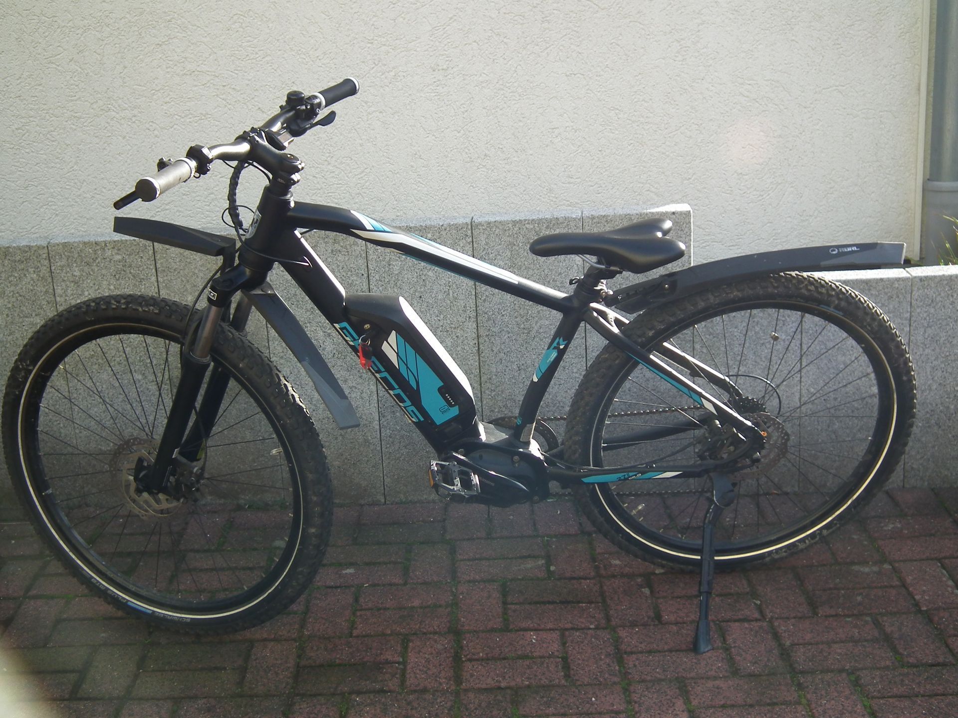 Ein schwarz-blaues Fahrrad steht auf einem gepflasterten Gehweg