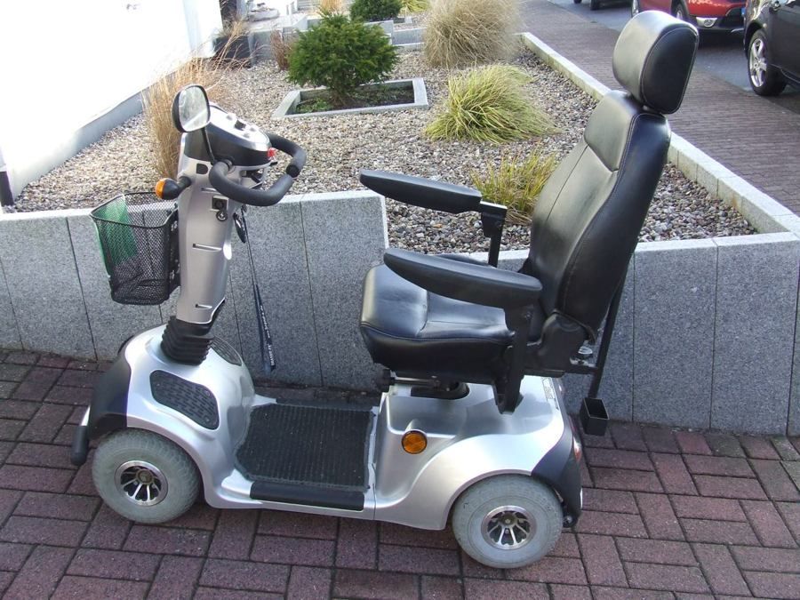 Ein silberner Elektromobil steht auf einem gepflasterten Gehweg