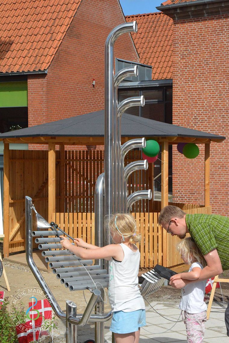 Lapset leikkivät korkealla metallisella liukumäellä puisen leikkimökin vieressä pihalla