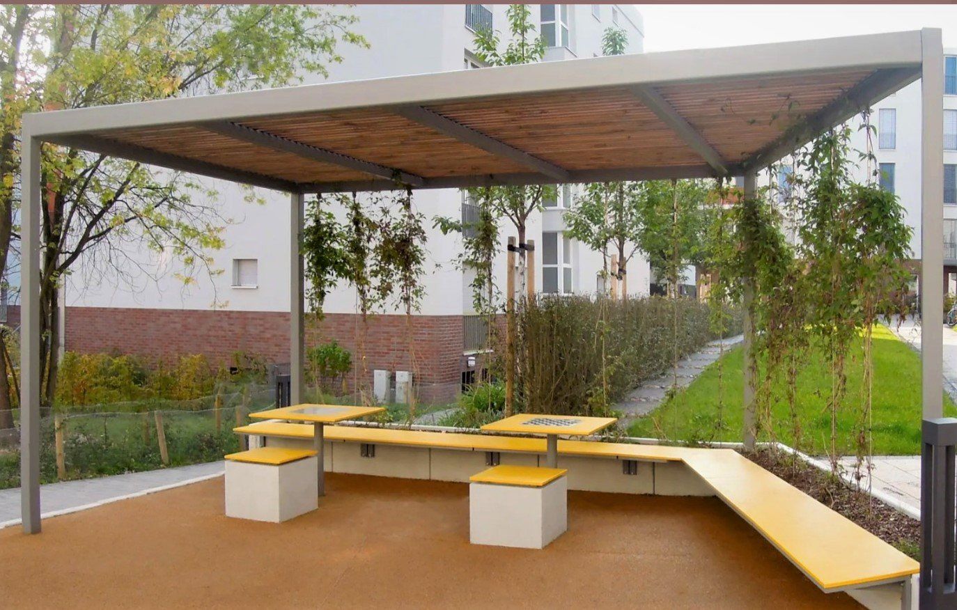 Ulkona oleva patio, jossa on puinen katos, keltaiset penkit ja ympäröivä vehreys