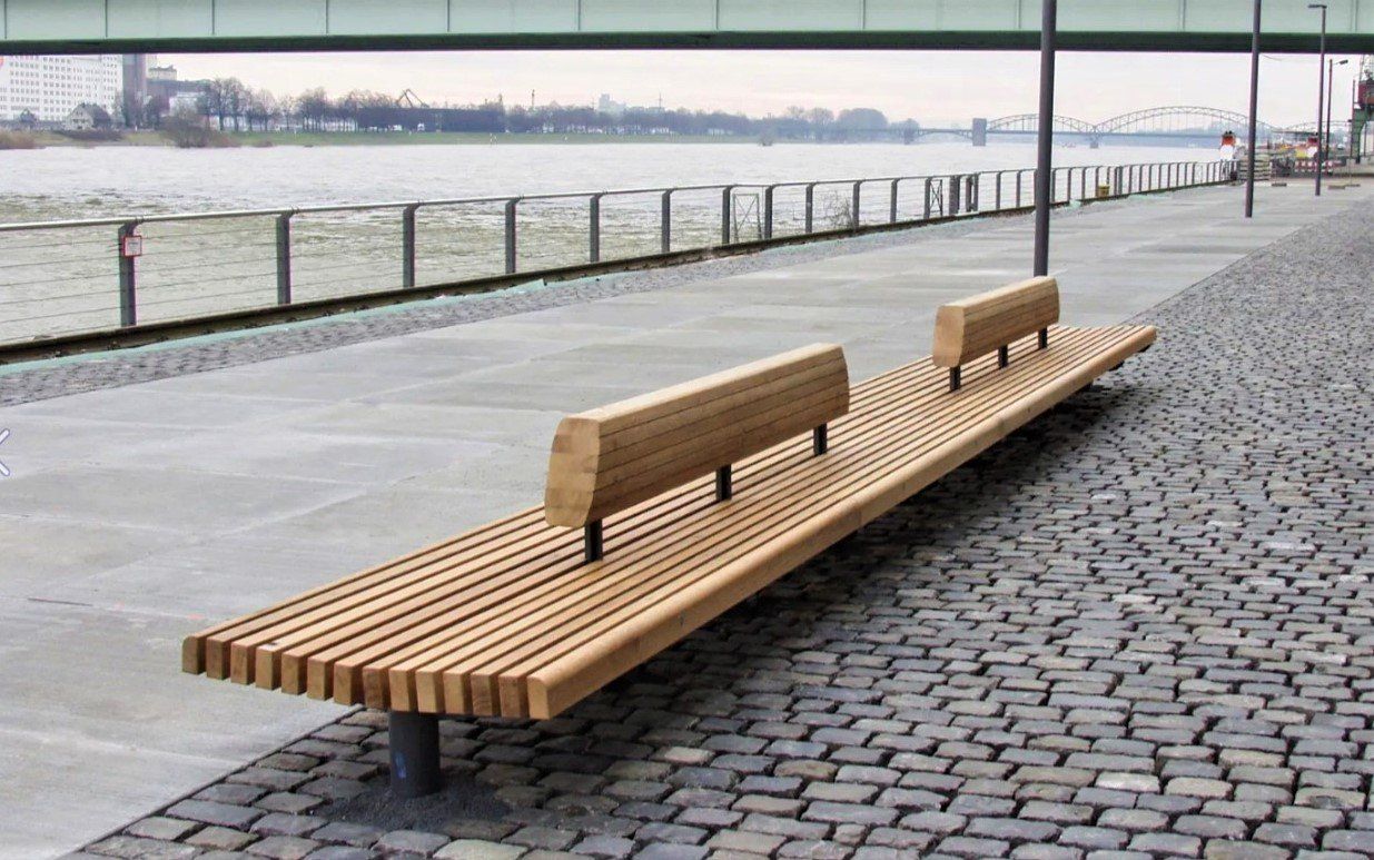 Pitkä puinen penkki jokirantapromenadilla, jonka lähellä on mukulakivipolku ja kaiteita