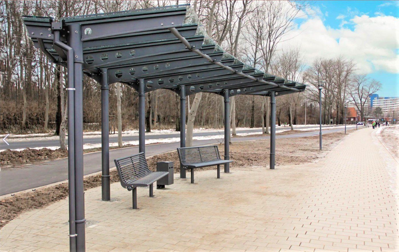 Puistopolku, jolla on pitkä metallinen pergola ja penkkejä lumisen tien ja paljaiden puiden vieressä.