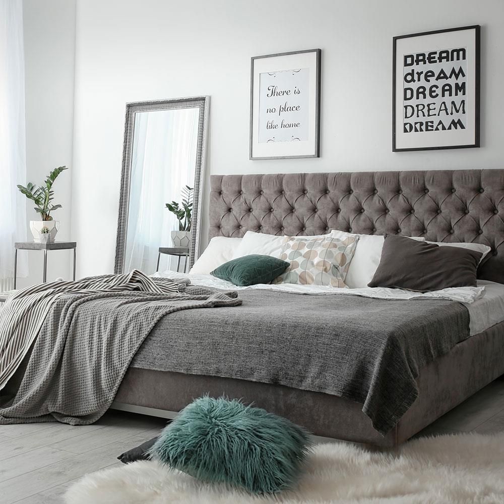 Ein Schlafzimmer mit Bett, Spiegel, Kissen und Postern an der Wand.