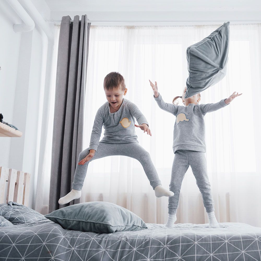 Zwei Kinder springen auf einem Bett mit Kissen herum.