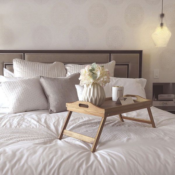 Ein Holztablett mit einer Vase mit Blumen darauf steht auf einem Bett