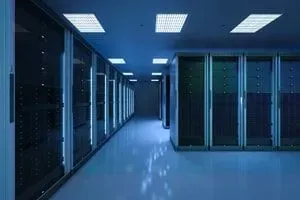Corredor do data center com fileiras de racks de servidores, iluminados com luz azul fria.