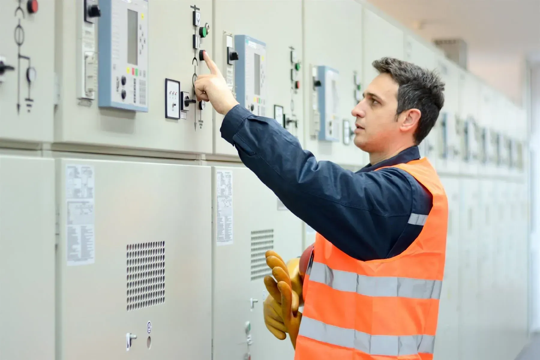 Homem com colete de segurança operando painel elétrico.
